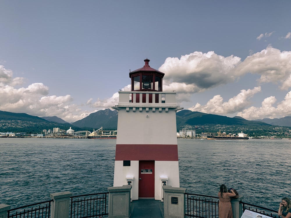 white and red concrete lighthouse near body of water during daytime