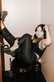 A softly lit photo of a college girl in casual clothes, seated comfortably on a toilet with a playful smirk.