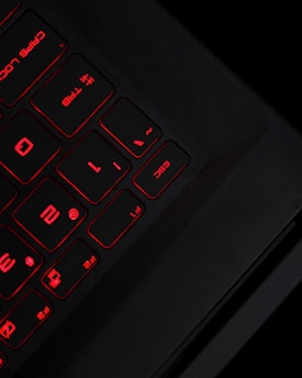 A close-up view of a keyboard with black keys illuminated by red backlighting. The keys for caps lock, escape, and the tab key are prominently visible, along with number and function keys. The lighting creates a futuristic and sleek appearance.
