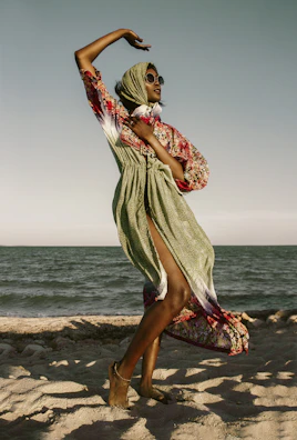 Model wearing a light, flowy summer dress paired with aqua shoes by the shore.