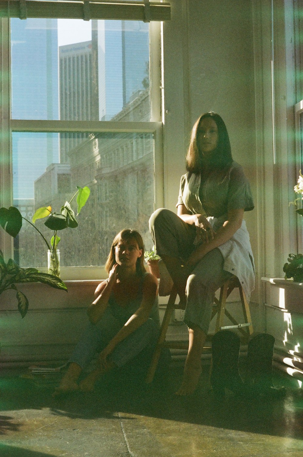 two women sitting on a chair in front of a window