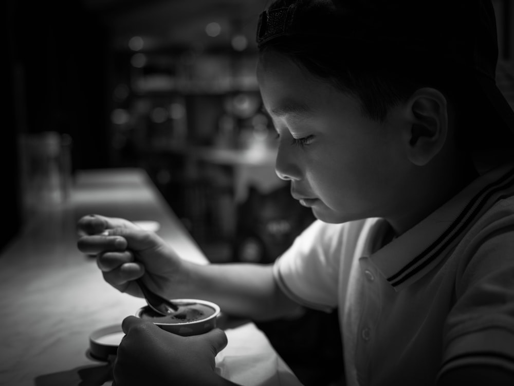 um menino sentado em uma mesa com uma colher na mão