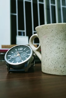 Pink dial watch catching sunlight on a city café table, surrounded by a coffee cup and a book.