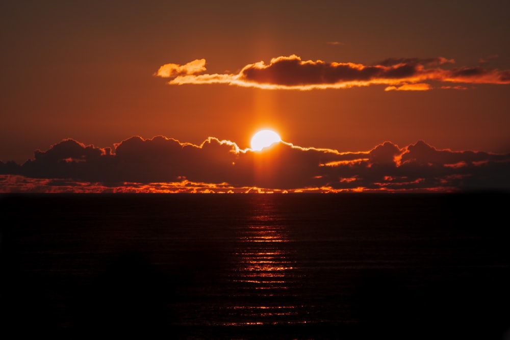 the sun is setting over the ocean with clouds