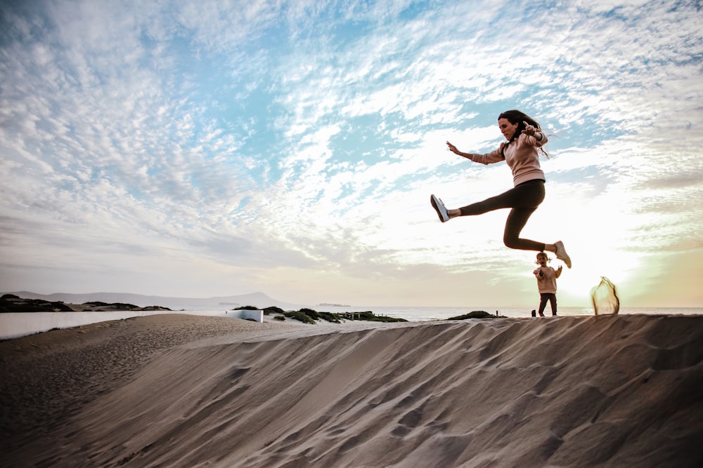 a woman is jumping in the air on a sand dune