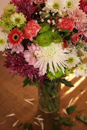 A vibrant bouquet of mixed fresh flowers in a rustic vase on a wooden table.