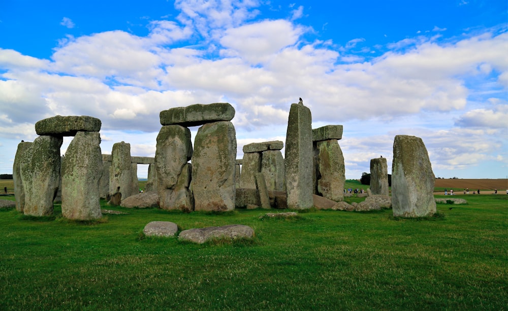 a stonehenge in a grassy field under a cloudy blue sky