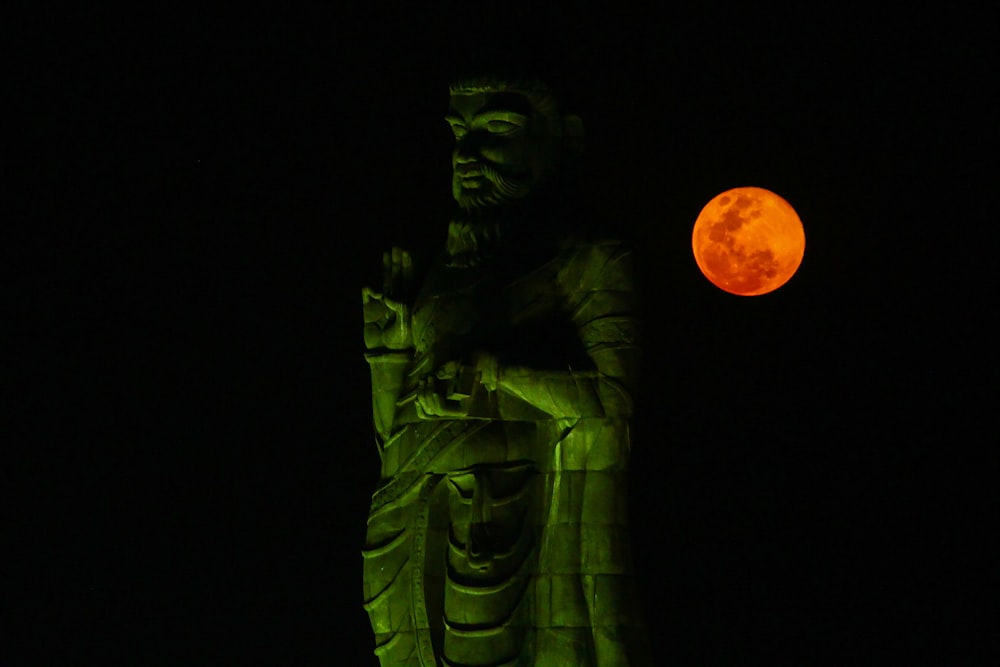 Une statue avec une lune rouge en arrière-plan