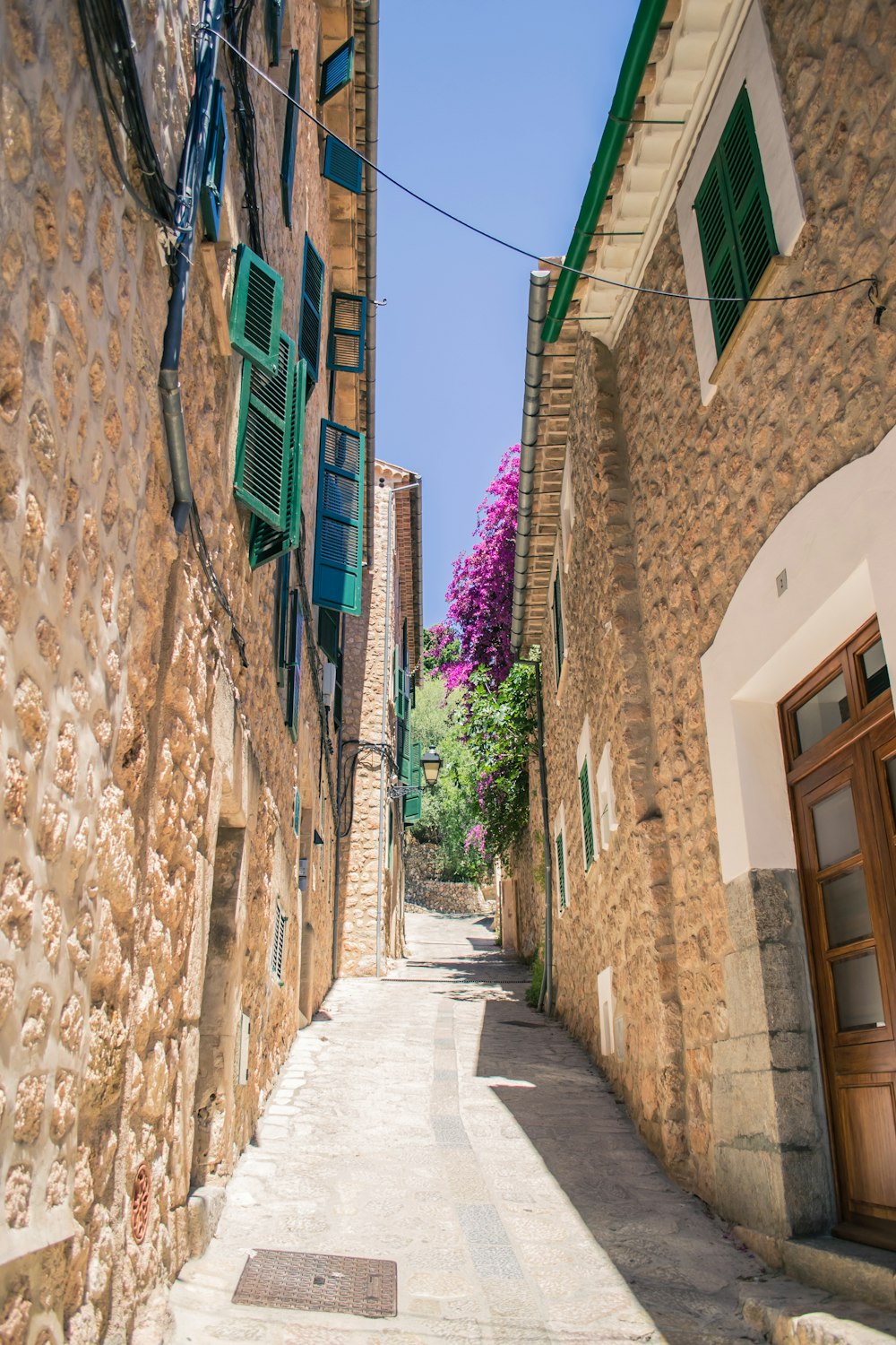 a narrow street with a stone building and green shutters