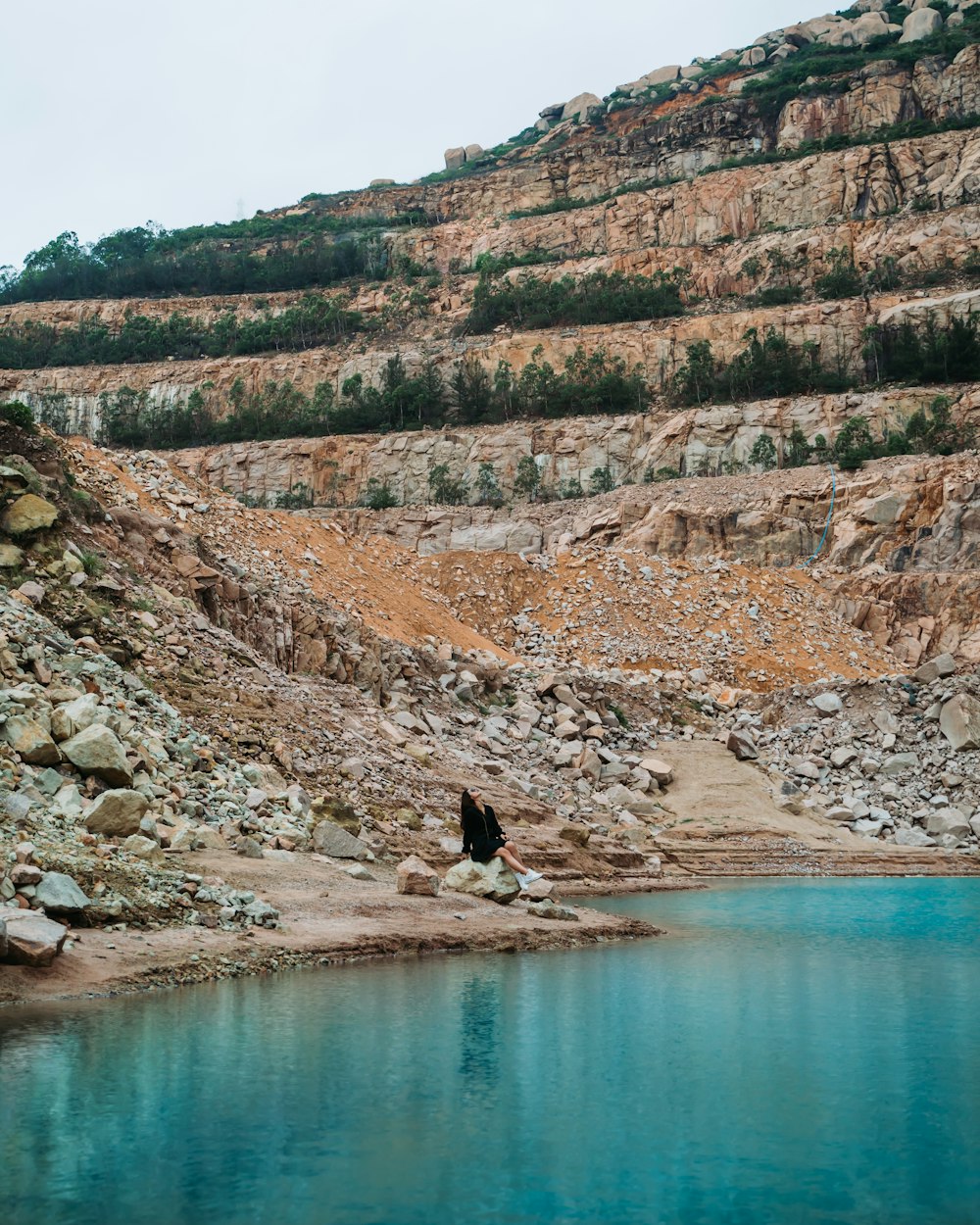 a person sitting on a rock near a body of water