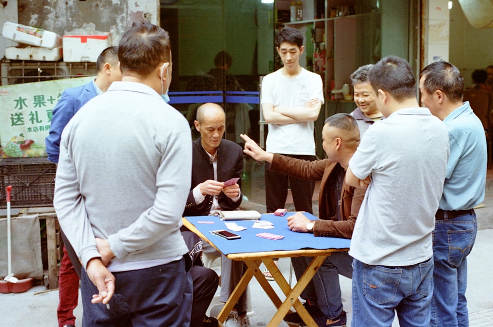 a group of men standing around a table playing cards