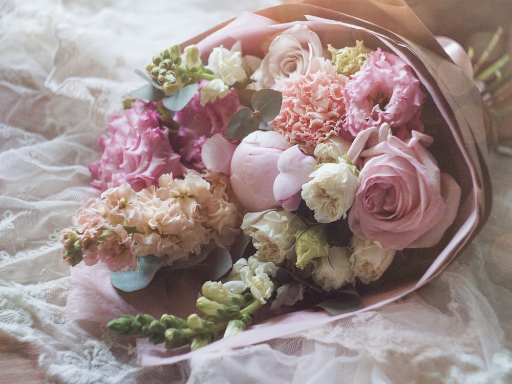 ein Strauß rosa und weißer Blumen, die auf einer mit Spitze bedeckten Oberfläche liegen