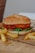 A crispy chicken burger sits on a vintage-style paper, adorned with sesame seeds on a fluffy bun. Inside, layers of fresh tomato and lettuce are visible, creating a delicious contrast with the golden-brown chicken fillet. Crispy french fries accompany the burger, enhancing the appetizing presentation.