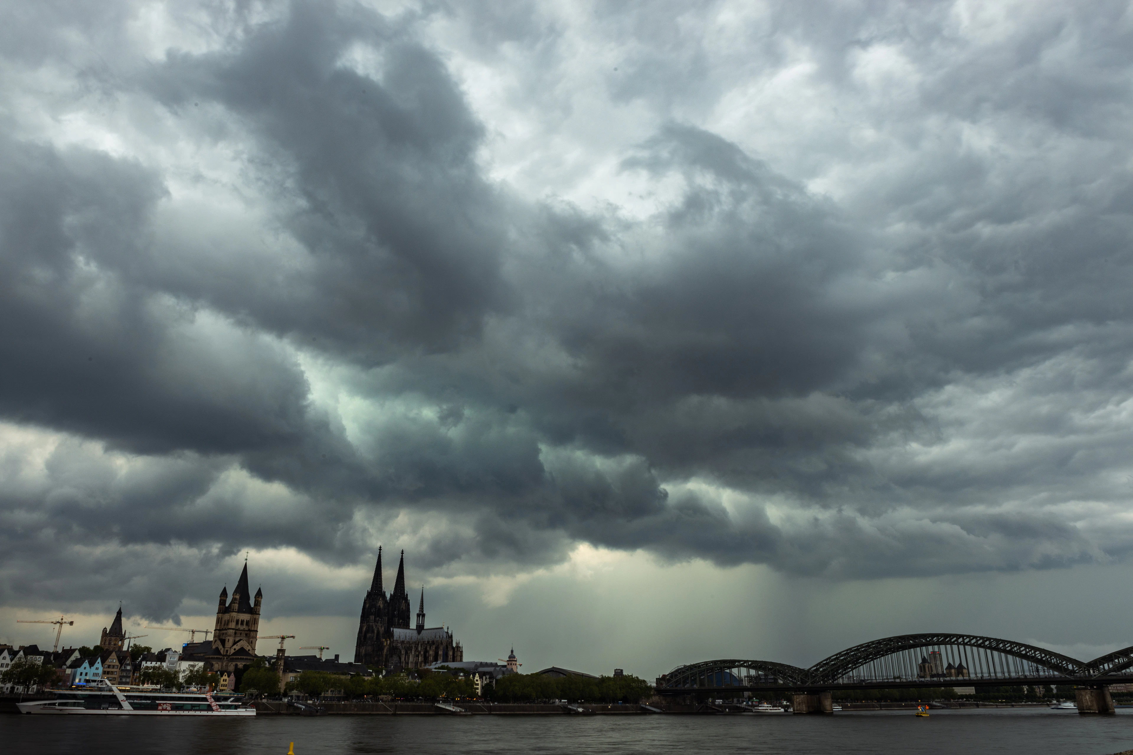 Dramatic storm clouds gather over Cologne Cathedral and the Hohenzollern Bridge above the Rhine.