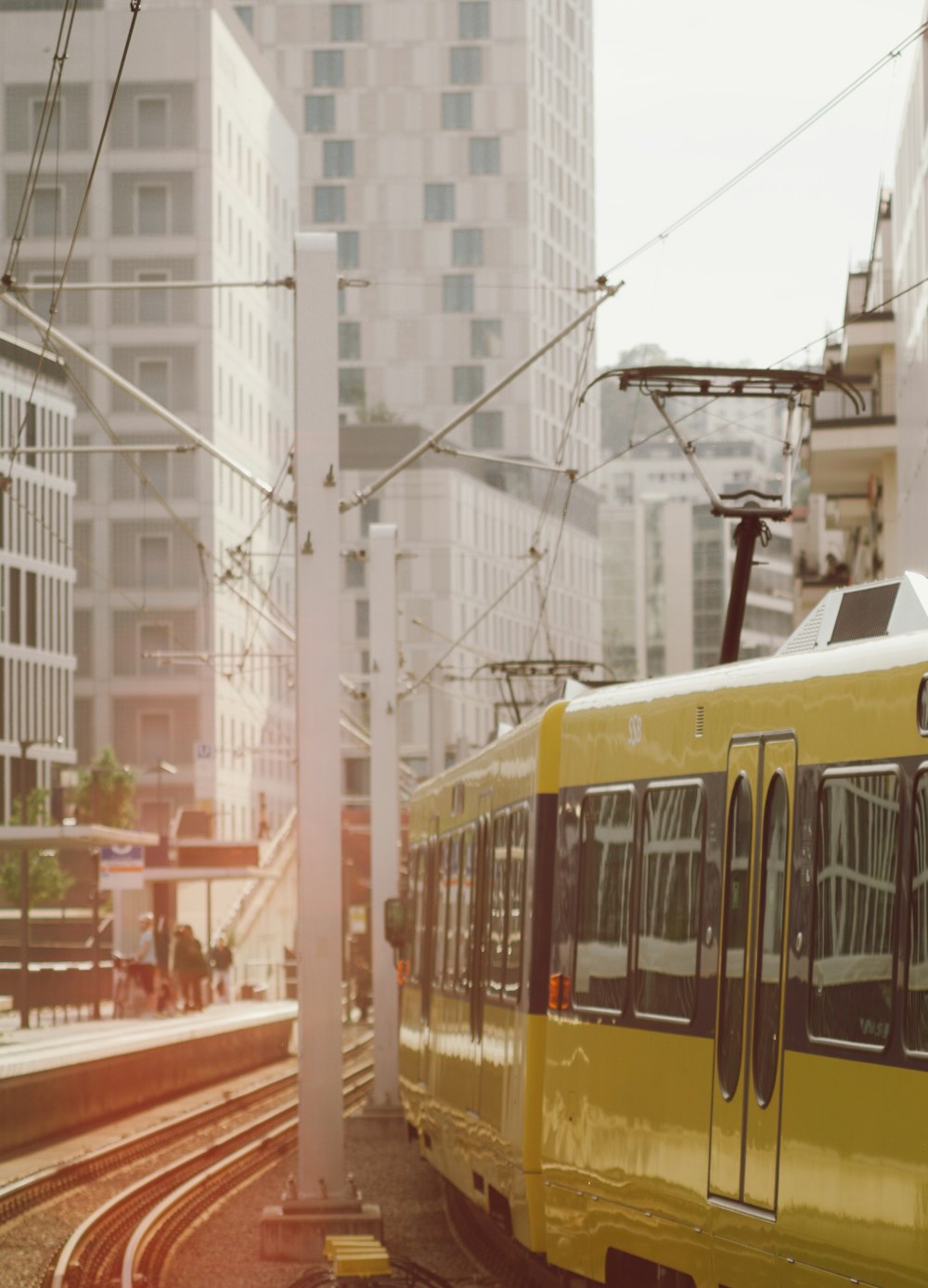 um trem amarelo viajando pelos trilhos do trem ao lado de edifícios altos