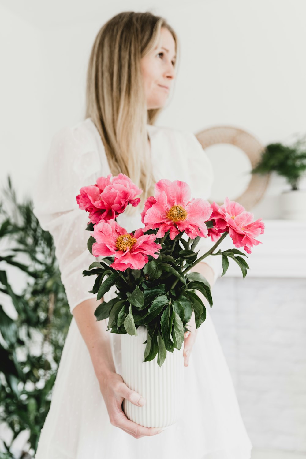 a woman holding a white vase filled with pink flowers