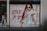 A fashion advertisement features a person with long braided hair wearing sunglasses and a denim outfit. The individual is making a bold gesture with their hand while standing against a wooden wall. The text 'GIVE ME A SMILE' is prominently displayed in red, along with a hashtag and the website URL 'tally-weijl.com'.