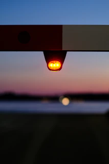 A solar-powered blinker flashing atop a boom barrier at an entrance gate during dusk.