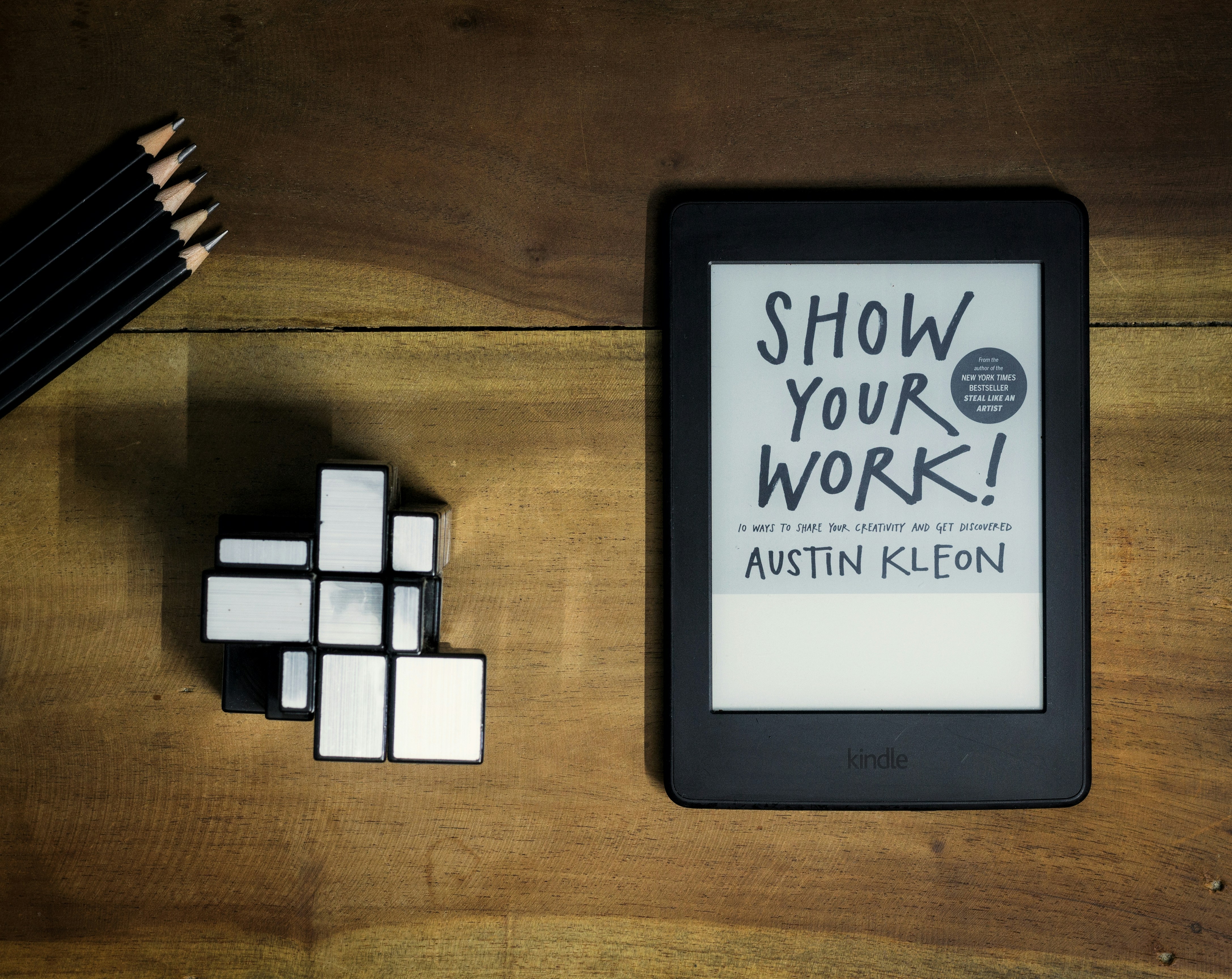 Amazon Kindle Paperwhite sitting on a modern wooden desk beside an Android smartphone