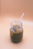 Freshly brewed iced coffee in a glass mason jar with a striped straw, set on a sandy beach table.