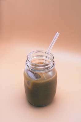 Freshly brewed iced coffee in a glass mason jar with a striped straw, set on a sandy beach table.
