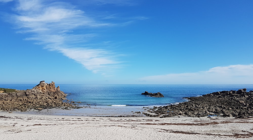 a sandy beach next to the ocean under a blue sky