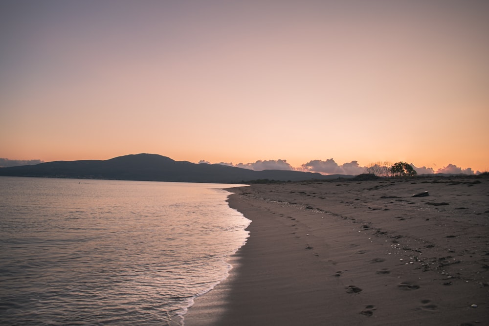 a beach at sunset with footprints in the sand