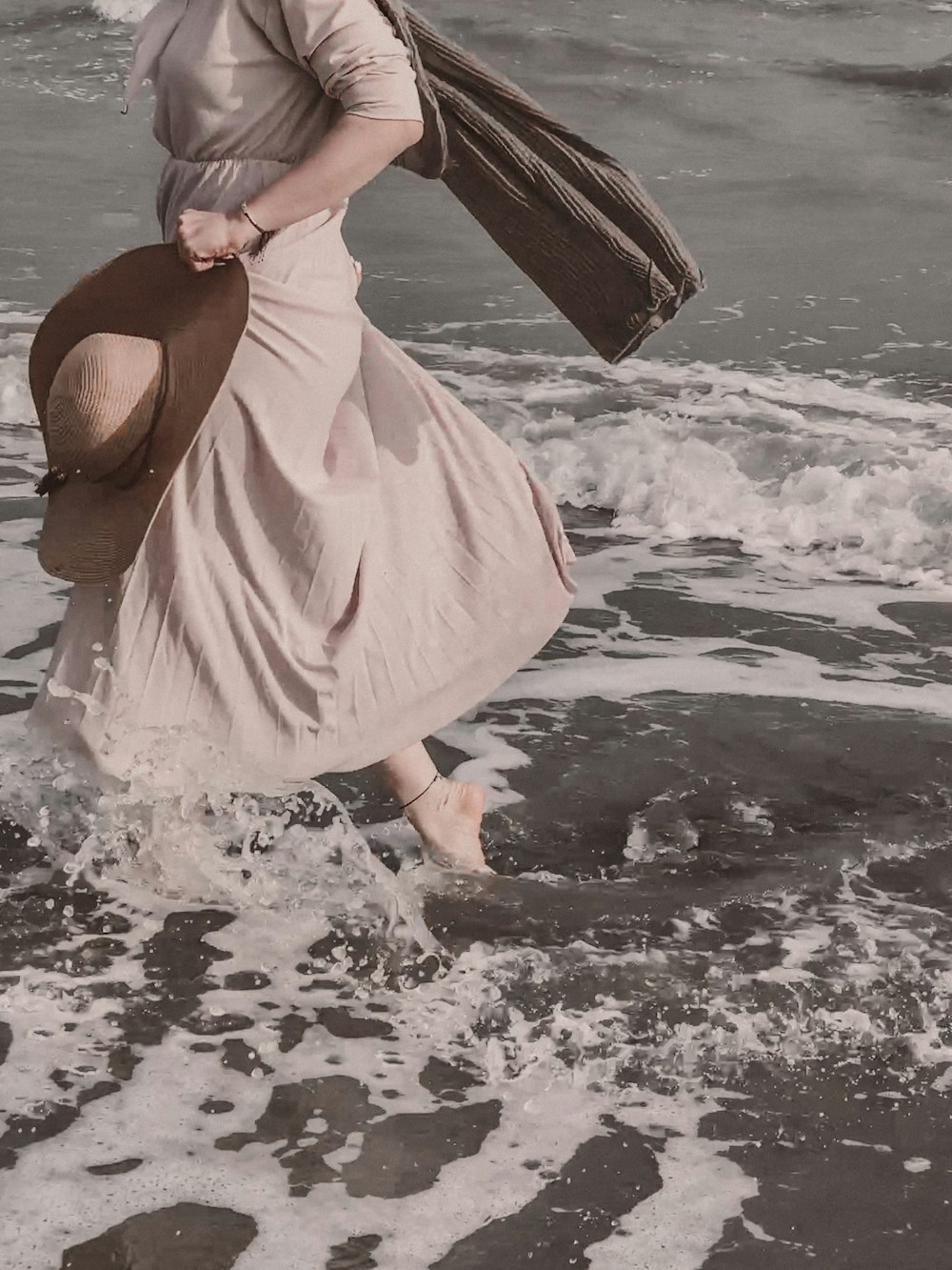 a woman in a dress and hat walking on the beach