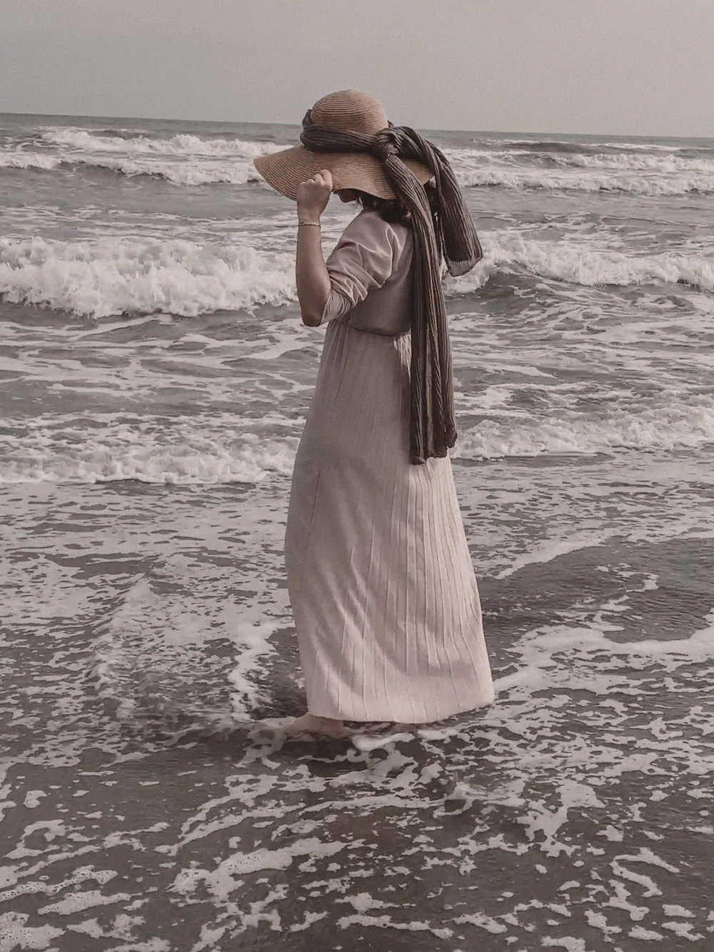 Mujer con vestido claro y sombrero de paja de pie en el mar