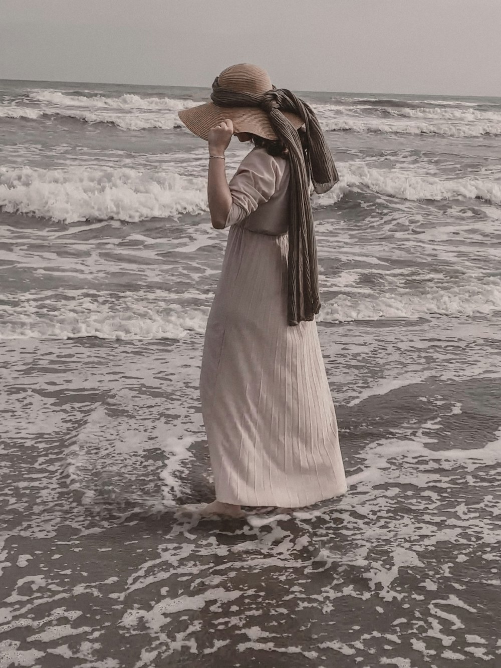 a woman in a dress and hat standing in the ocean