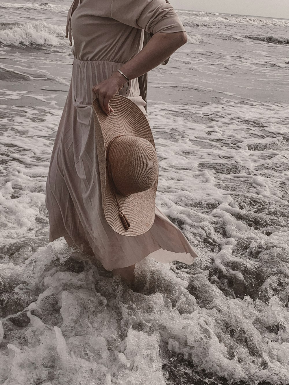 a woman standing in the ocean with a hat