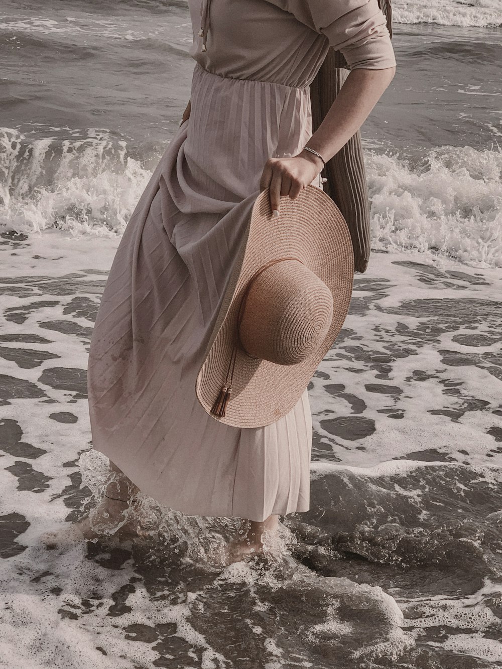 a woman in a dress and hat walking into the ocean