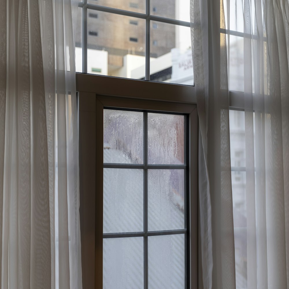 a window with white curtains and a view of a city