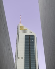 A tall, modern skyscraper with a prominent glass facade and a sharp, angular design. The building is positioned between two other tall structures and features the logo 'SOUTH32' near its top. The sky is a pale, muted color, providing a stark contrast to the building's sleek surfaces.