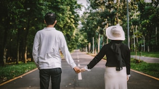 a man and woman holding hands while walking down a road