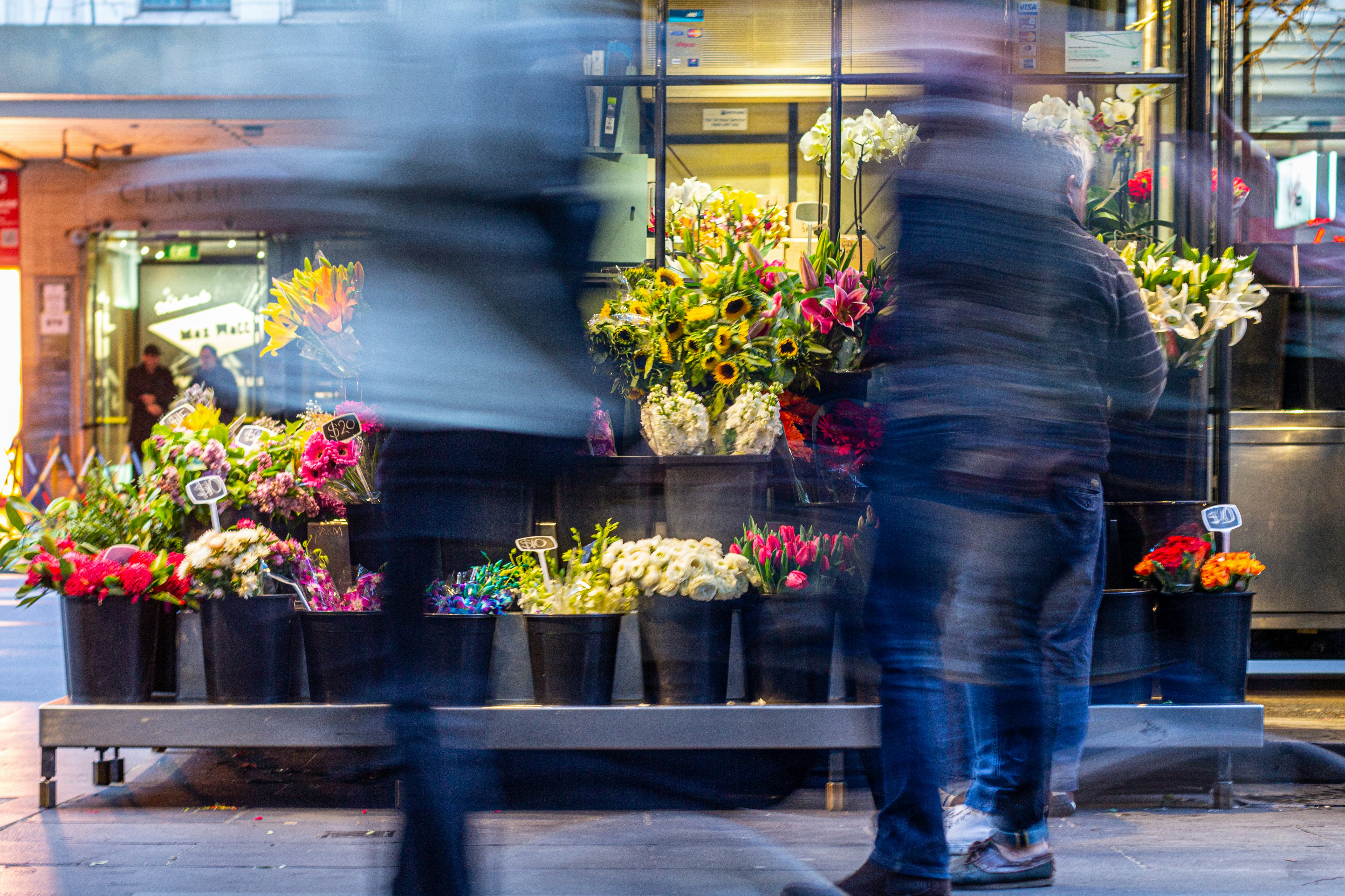a blurry photo of a man walking past a flower shop