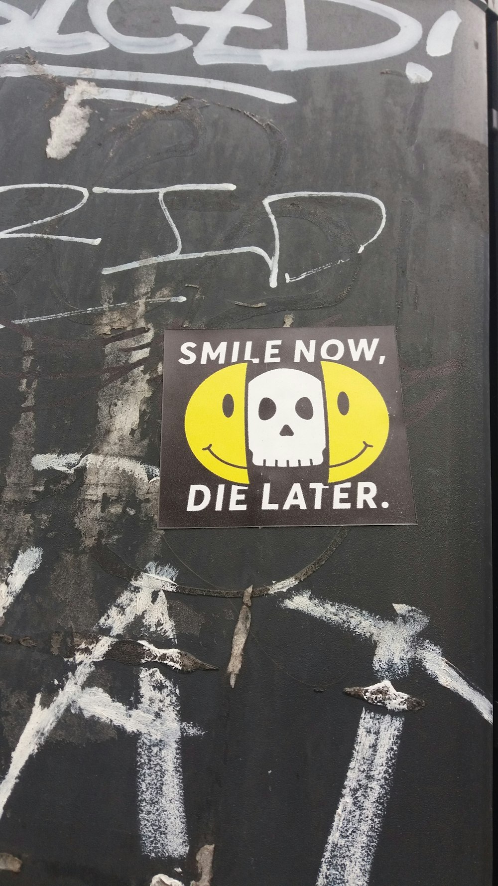 a sticker on the side of a wall that says smile now, die later