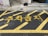 Yellow paint marks the words in Korean characters on a dark asphalt surface, framed by diagonal lines indicating a restricted parking area. The background features part of a building, a tire, and some urban elements.