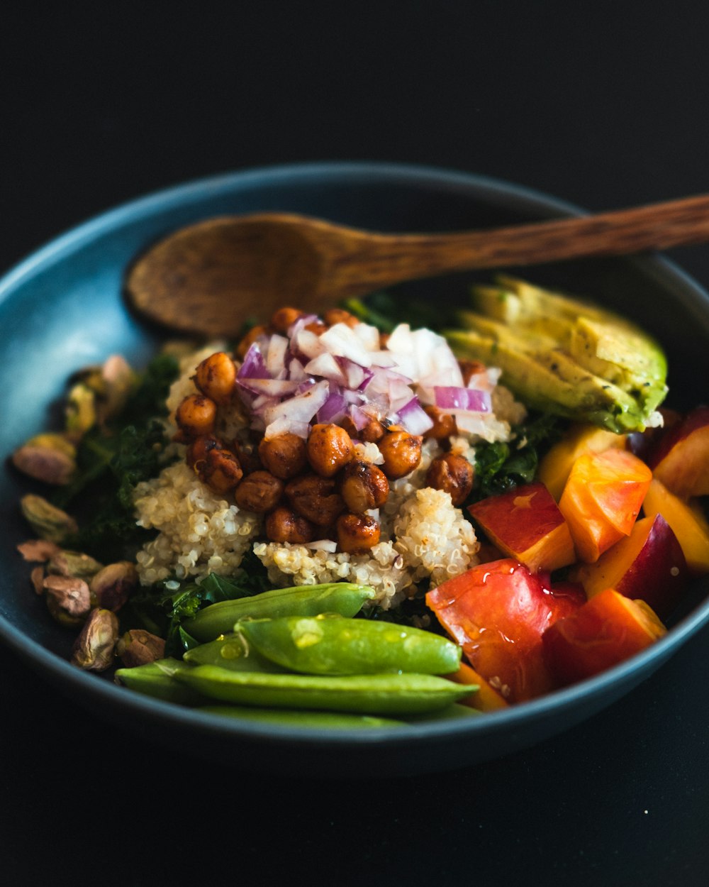 a blue bowl filled with vegetables and a wooden spoon