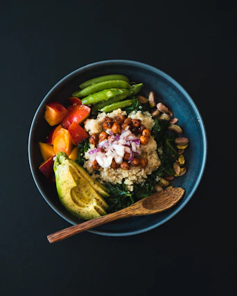 a blue bowl filled with vegetables and a wooden spoon