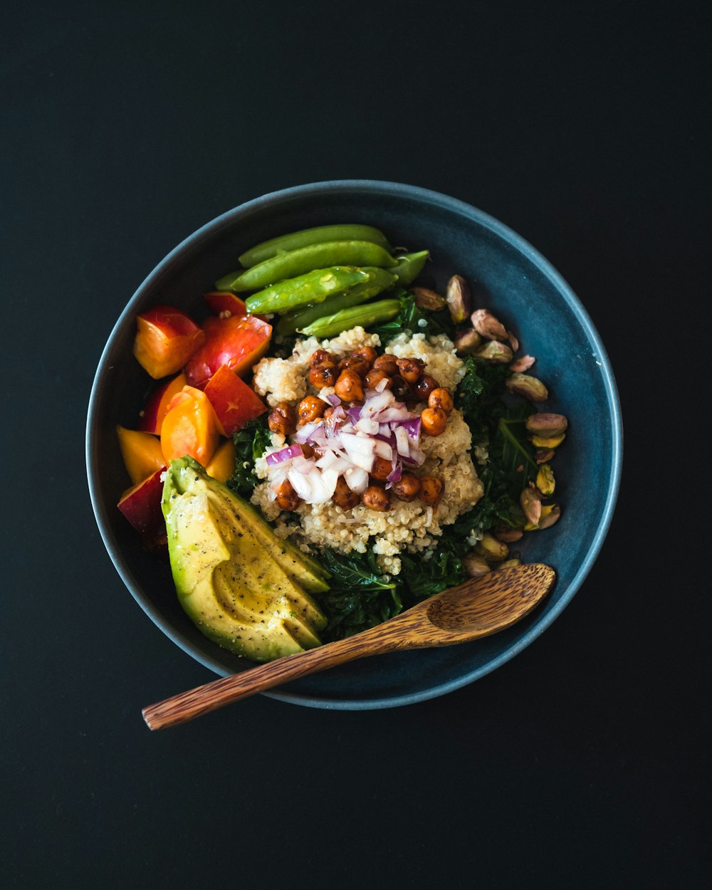 a blue bowl filled with vegetables and a wooden spoon