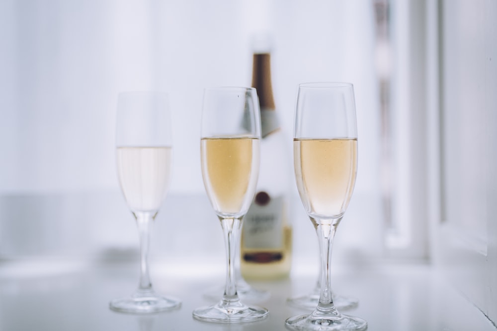 Tre bicchieri di champagne seduti accanto a una bottiglia di vino