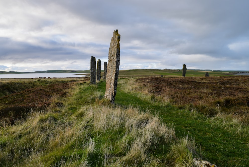 a stone monument in a grassy field with a body of water in the background