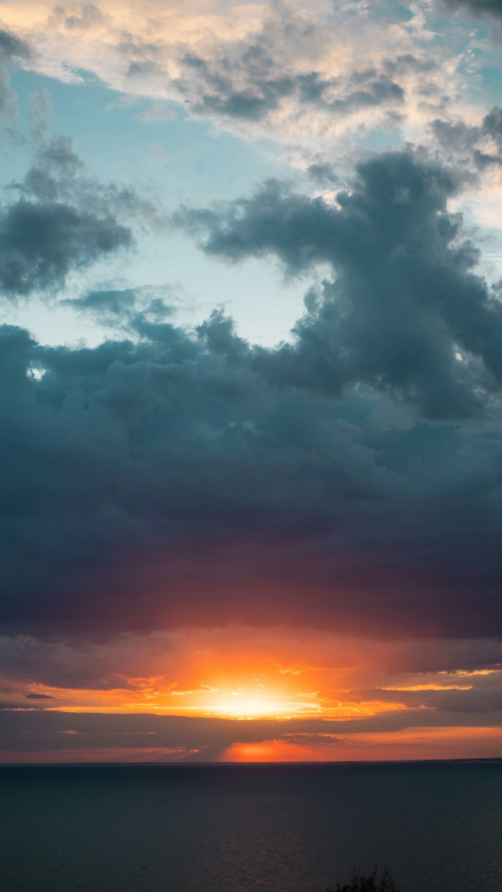 the sun is setting over the ocean on a cloudy day