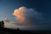 a large cloud is in the sky above a hill