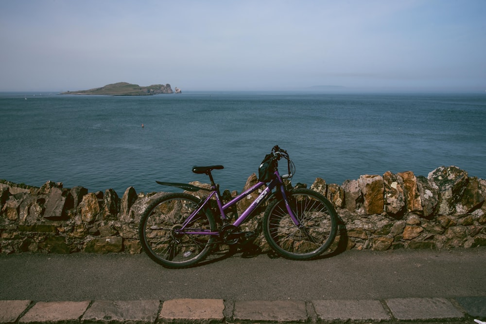 a purple bike parked next to a stone wall