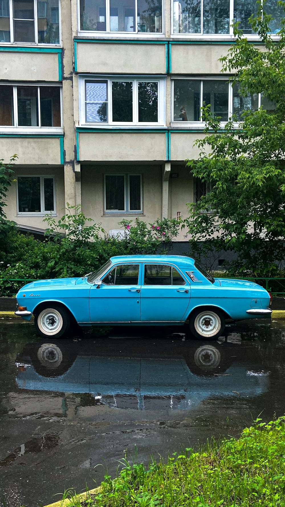 a blue car parked in front of a tall building