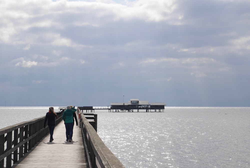 two people walking down a pier towards the ocean