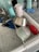 A kitchen sink with a drying rack containing various kitchen items including a stainless steel pot, a plastic container, a cup, and kitchen utensils. Nearby, there are cleaning supplies like dish soap, a sponge, and hand sanitizer on a tiled countertop.