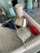 A kitchen sink with a drying rack containing various kitchen items including a stainless steel pot, a plastic container, a cup, and kitchen utensils. Nearby, there are cleaning supplies like dish soap, a sponge, and hand sanitizer on a tiled countertop.